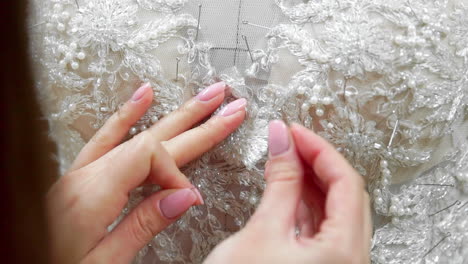 diseñador de moda de primer plano para novias en su estudio alfileres agujas encaje vestido de novia. costurera crea un vestido de novia exclusivo. seguro con alfileres y agujas contorno. pequeño negocio privado. coser rhinestones y cristales al hilo del vestido y aguja. trabajo de joyería.