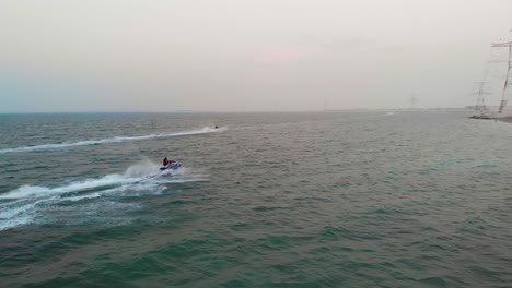 Drone-chases-to-JetSki's-speeding-through-green-Abu-Dhabi-ocean-waters-on-hazy-day,-Aerial