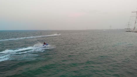 drone chases to jetski's speeding through green abu dhabi ocean waters on hazy day, aerial