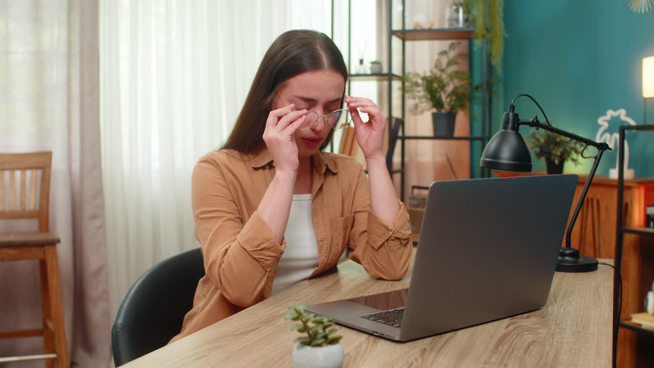 Young woman removing glasses rubbing tired eyes after long laptop work feeling relief and eye strain