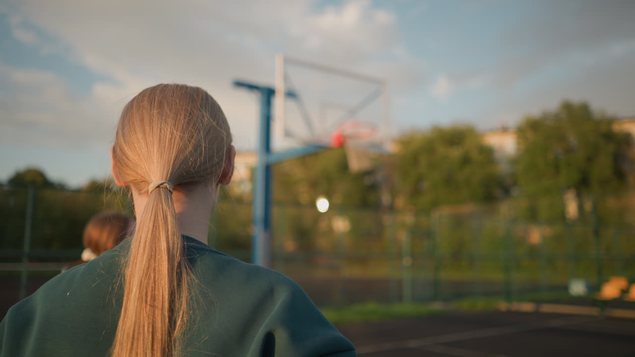 미소 짓고 볼리볼을 하는 두 여인의 클로즈업, 배경에 농구 허프, 나무와 건물을 볼 수 있으며, 활기찬 야외 환경을 만니다.