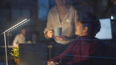 businesswoman bringing coffee to colleagues working together at night in office