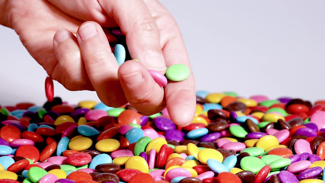Close-up view of hands interacting with a colorful assortment of small, round candies.