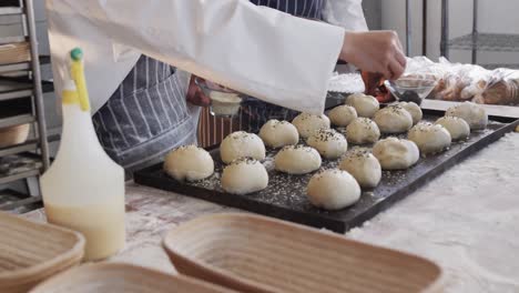 diverse bakers working in bakery kitchen, sprinkling poppy seeds on rolls in slow motion