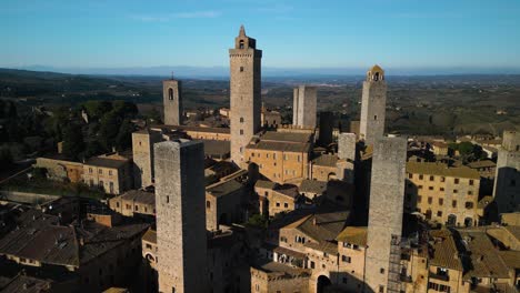 Boom-Shot-Zeigt-Mittelalterliche-Türme-In-San-Gimignano-Mit-Toskanischer-Landschaft-Im-Hintergrund