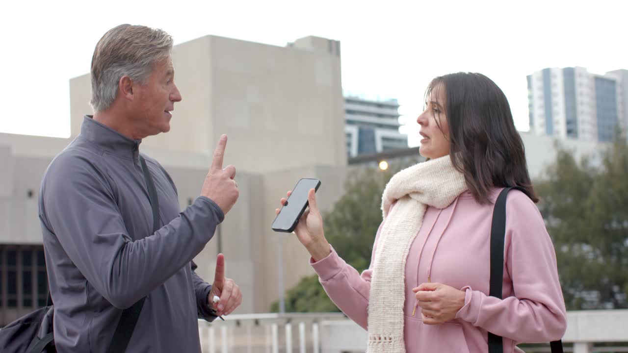 Diverse friends demonstrating earbud pairing on rooftop terrace after phone offer, tapping screen