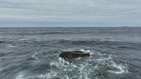 Wellen-Spülen-über-Einen-Schwarzen-Felsen-Entlang-Der-Südküste-Islands-–-Im-Hintergrund-Ist-Der-Atlantische-Ozean-Zu-Sehen