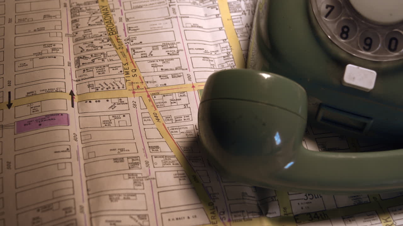 Jevn kamerabevegelse som avslører en retro grønn skivetelefon som hviler på et papirkart over New York. Kriminaldetektiv, reiseplanlegging eller noir-etterforskning
