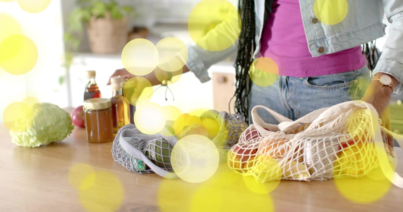 Reaching into mesh bag, woman unpacking glass jars and water bottle in kitchen for meal prep