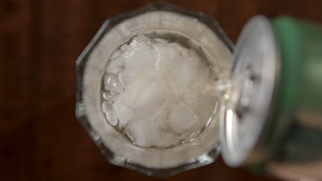 slow motion shot of hand pouring soda liquid into glass with cold ice cubes inside bar