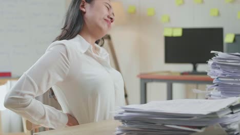 close up of asian woman having backache while working hard with documents at the office