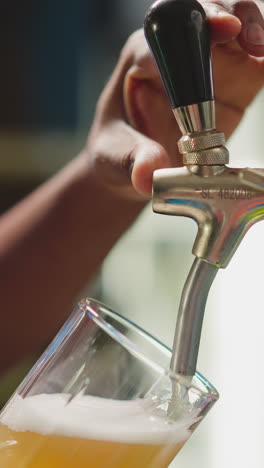 el camarero llena la taza con cerveza espumosa desde el grifo de primer plano. el trabajador de la cervecería afroamericano vierte bebida fresca en el vaso para los invitados. el hombre sirve cerveza artesanal