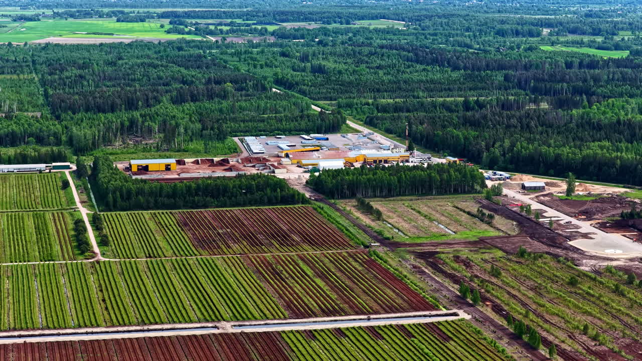 Aerial landscape of large peat fields and processing plant surrounded by green forest