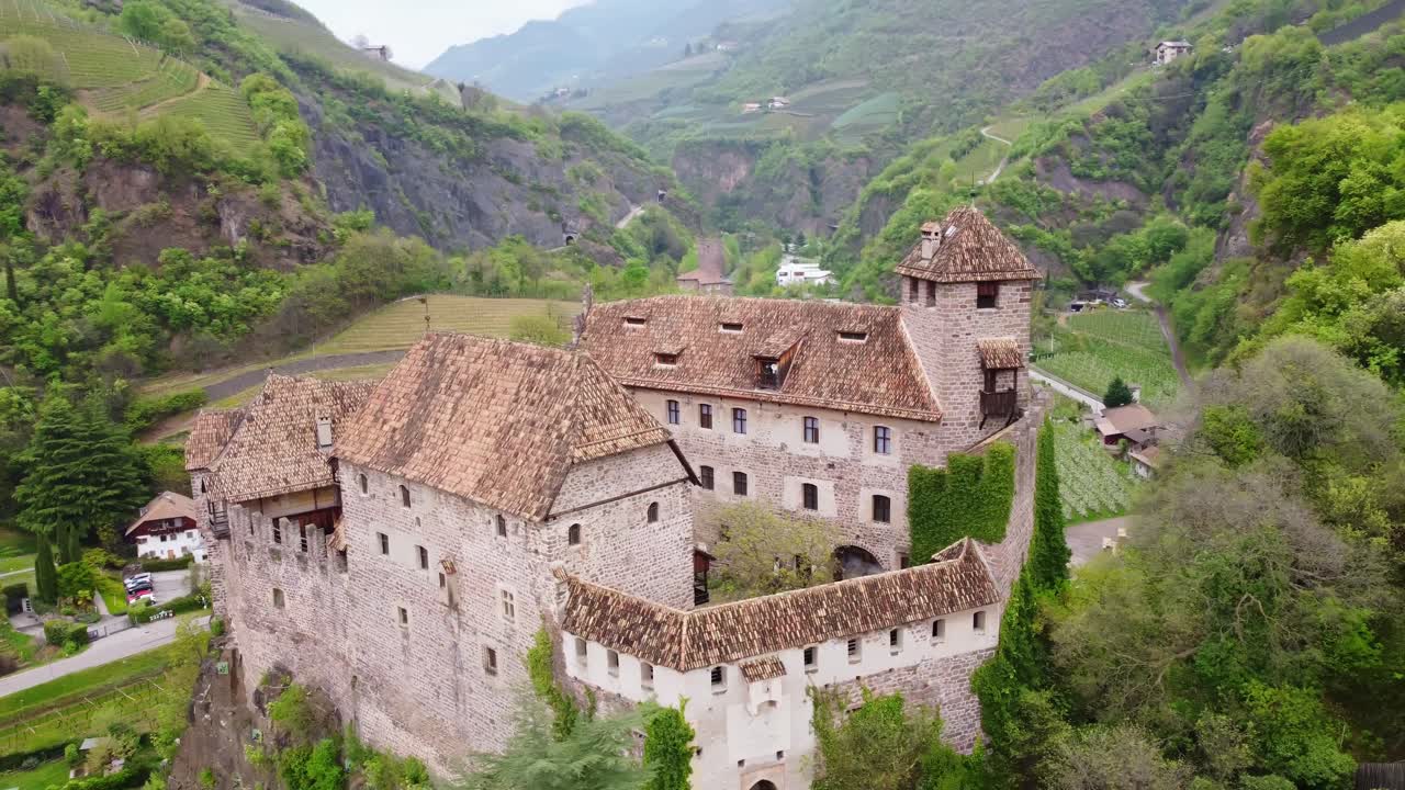 Drone circles above Roncolo Castle, revealing green mountain valleys and stunning Alpine scenery