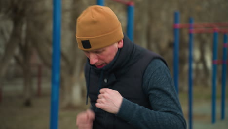 close-up of a coach working out at a fast pace, with a black car and a white car moving in opposite directions across the road behind him, with a barren trees in the background