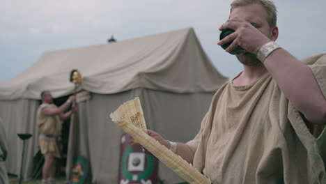 roman soldier drinking from a cup while studying a papyrus