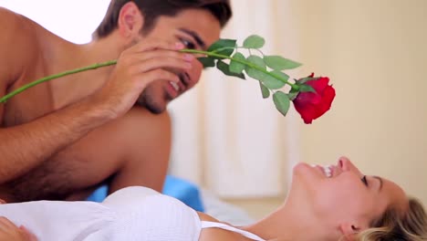 man tickling his pretty girlfriend with a red rose on bed