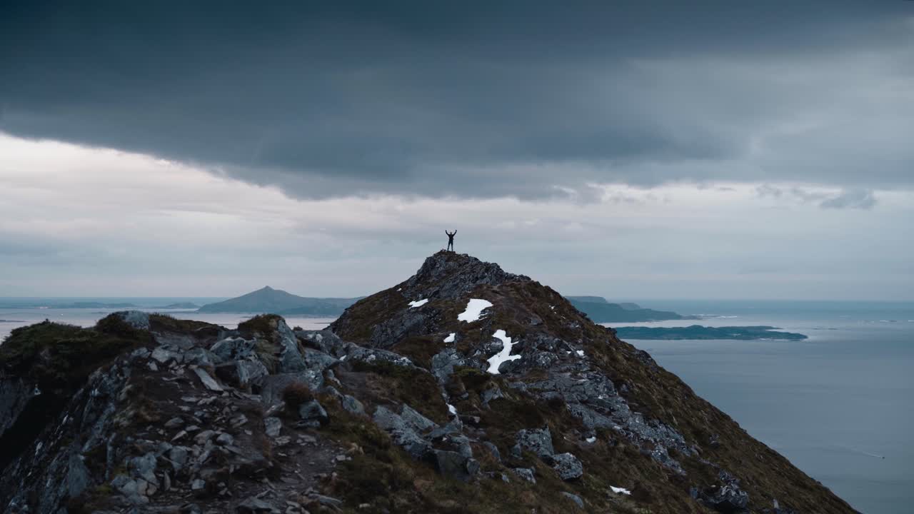 노르웨이의 바다 경치로 둘러싸인 공중에 팔을 들고 큰 산 꼭대기에 서있는 사람