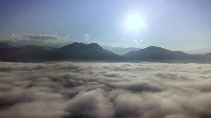 Slow aerial flight above the clouds towards mountains in the morning.