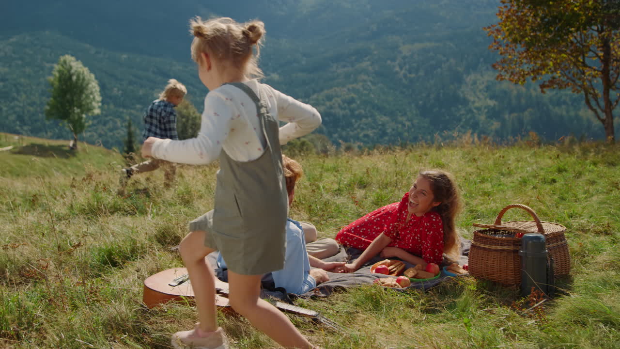 счастливый семейный пикник солнечный день на зеленом холме. дети бегают вокруг улыбающихся родителей