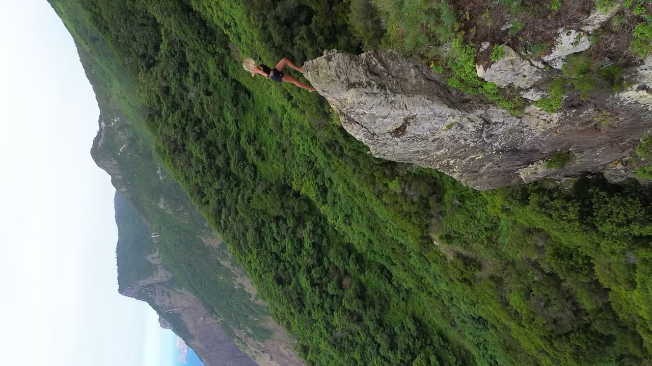 Beautiful blonde girl climbing high ridges cliff on the coast of Madeira Island, Portugal