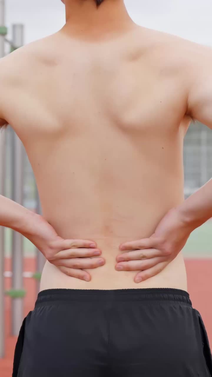 Young athlete with back pain holding his lower back, vertical video