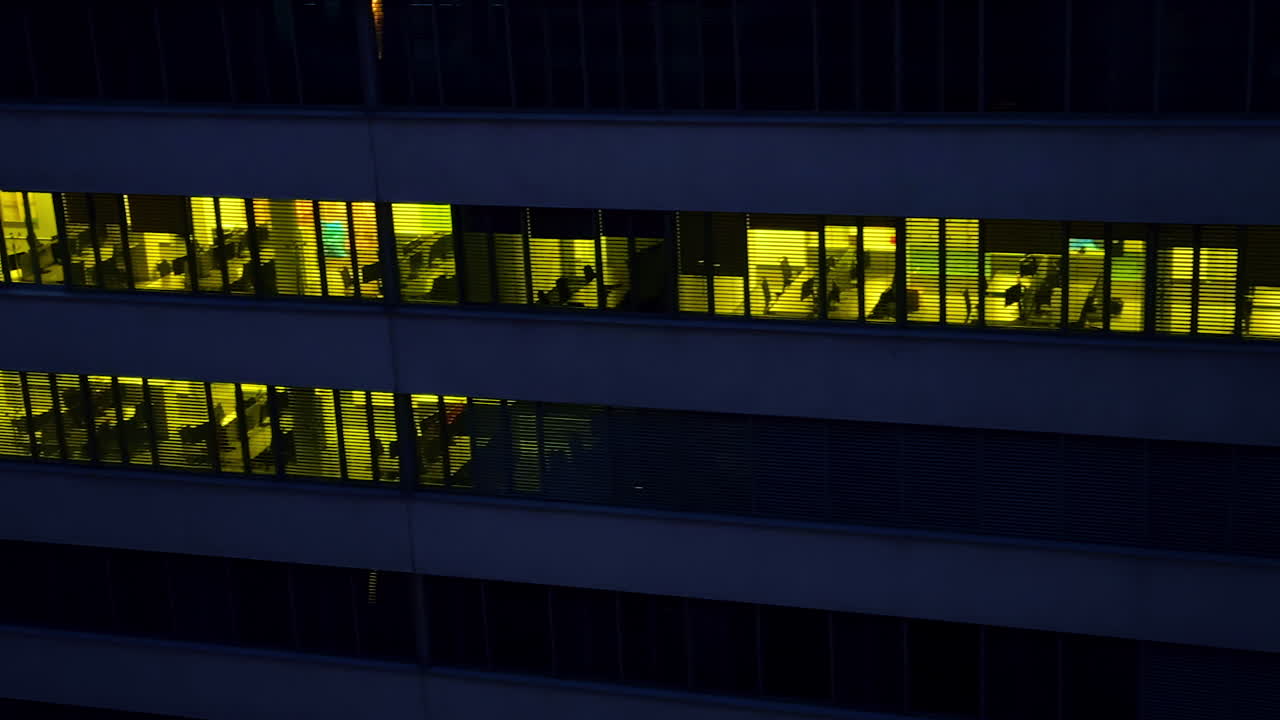 Footage at the facade of the office building at dark time of the day. Drone flight along the floors with light switched on in the rooms