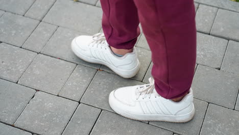 high angle view gym enthusiast in white sneakers and burgundy sports suit walking on gray interlocking tile pavement during outdoor workout session capturing stride movement and urban fitness routine