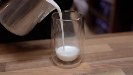 barista pouring frothed milk to a glass cup preparing a latte coffee