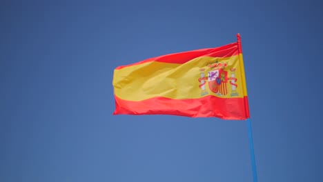 Bandera-Española-Ondeando-En-El-Viento-Contra-El-Cielo-Azul,-Tiro-De-ángulo-Bajo-En-Cámara-Lenta