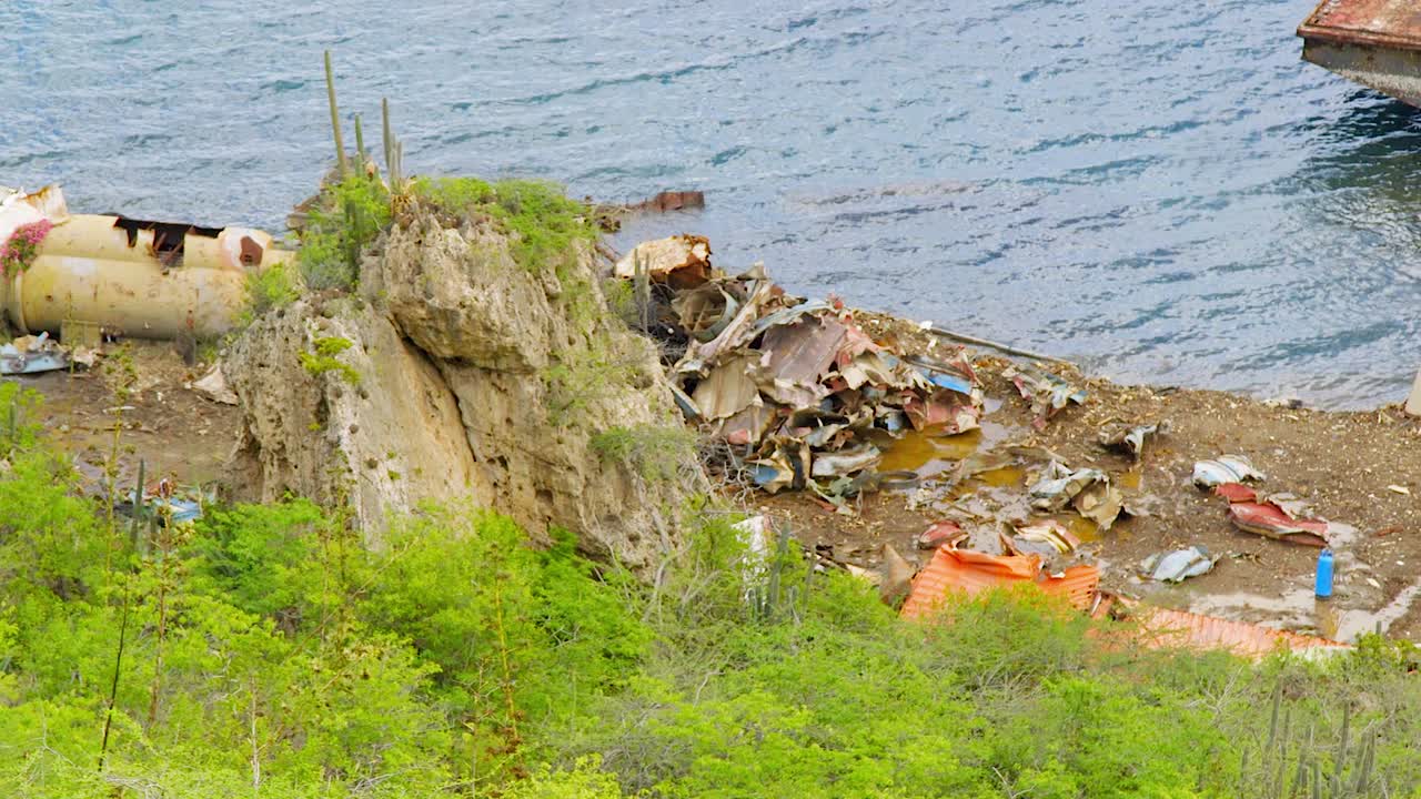 Metal scrapyard facility with rusty old boats by the water. Panning shot
