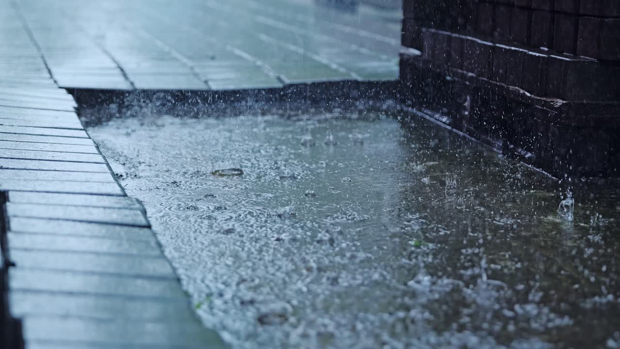 Dramatic rainfall close up in city, raindrops splashing on concrete patch