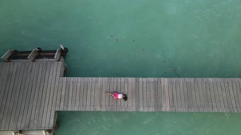 Aufsteigende-Luftaufnahme-Einer-Jungen-Ostindischen-Frau,-Die-Auf-Einem-Steg-Mit-Dem-Kristallklaren-Wasser-Der-Karibischen-Insel-Tobago-Liegt