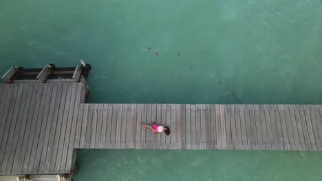 vista aérea ascendente de una joven india oriental recostada en un embarcadero con las aguas cristalinas de la isla caribeña de tobago debajo