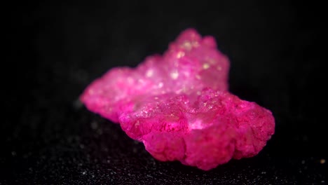 girando sin problemas un mineral rosado en forma de hogar frente a un fondo negro