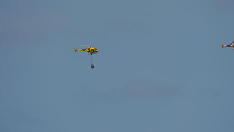 yellow helicopter flying with suspended red bambi bucket used for firefighting purposes
