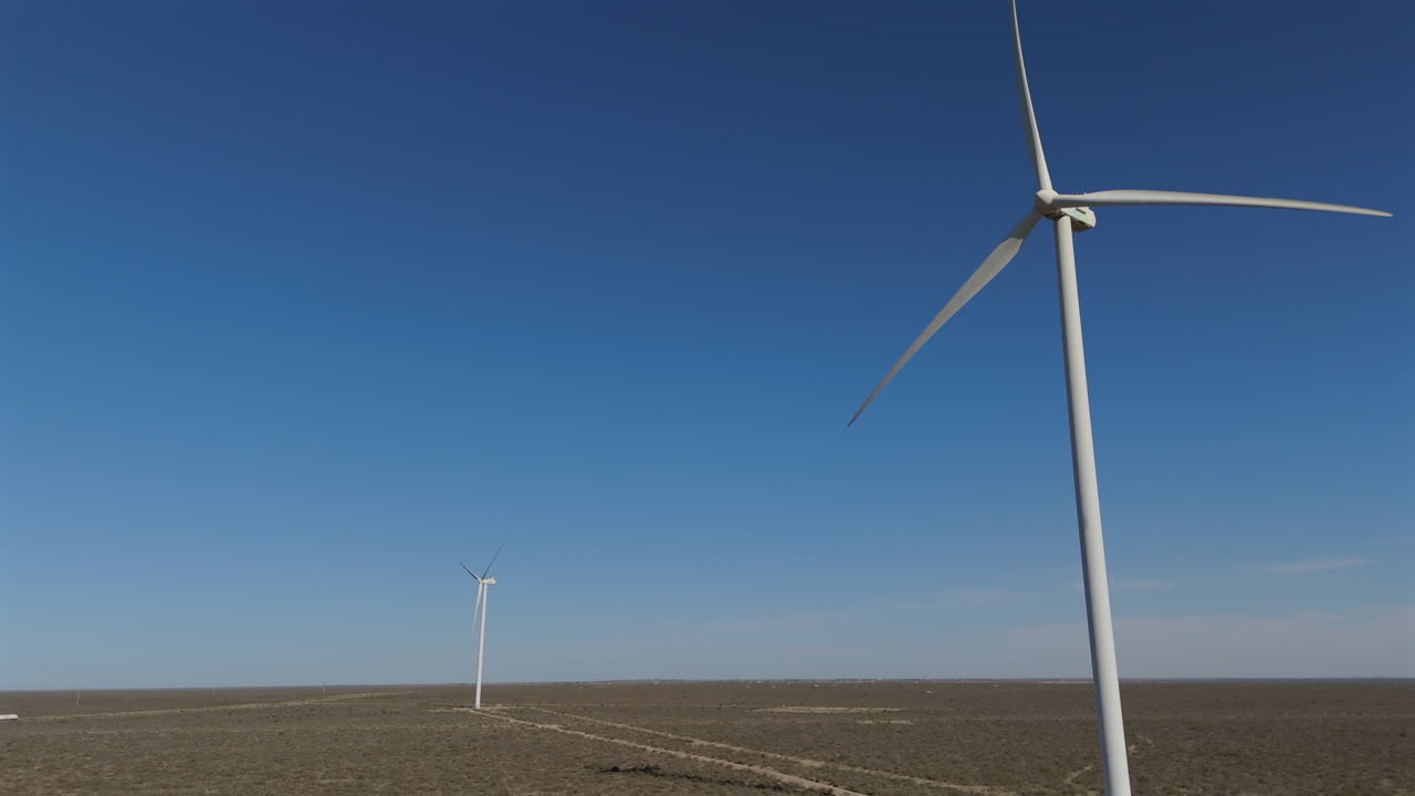 Slow motion aerial view descending in front of energy windmills at wind farm