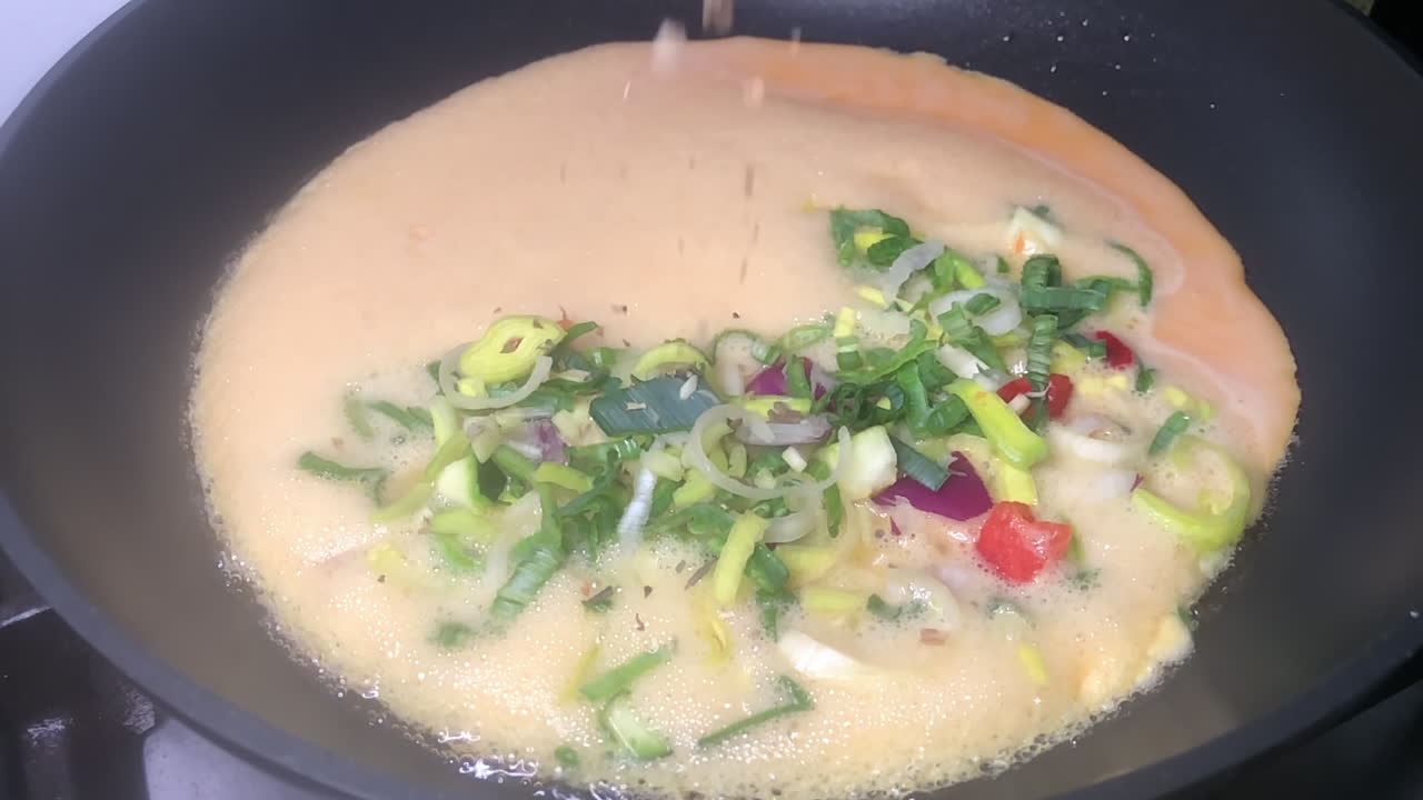 이탈리아 믹스에서 오레가노와 바질 허브의 극단적인 슬로우 모션 샷은 프라이팬에 있는 스페인 야채 오믈렛 위에 뿌려집니다.