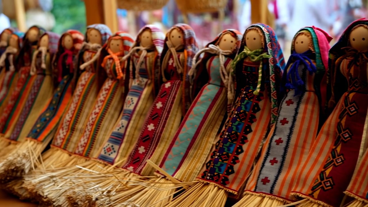 Uma fileira de bonecas de tecido artesanais usando vestidos estampados e lenços de cabeça está disposta em uma prateleira, com um fundo de mercado suavemente desfocado e iluminação interna quente.