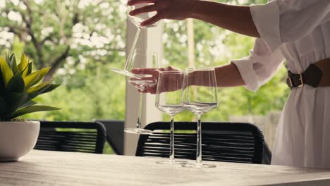 a woman setting down wine glasses on a dining table in an outdoor dining area