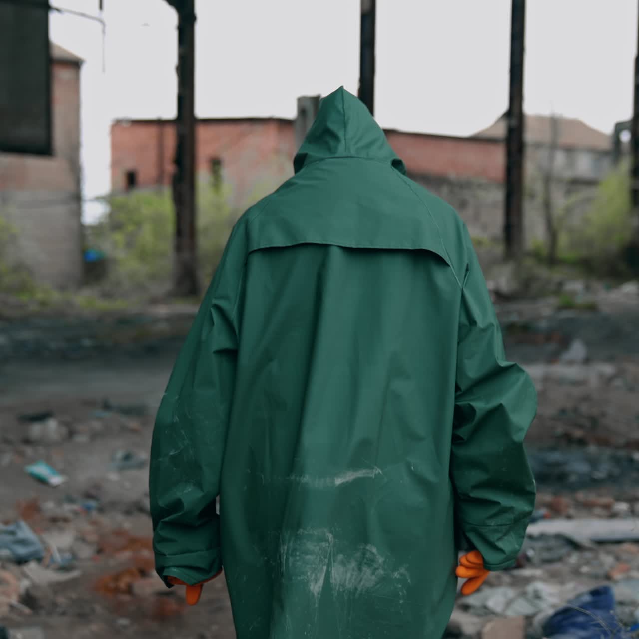 Person in post-apocalyptic place. Survivor in green hazmat suit with gas mask turns his head and looks at camera. Ruined place after chemical attack