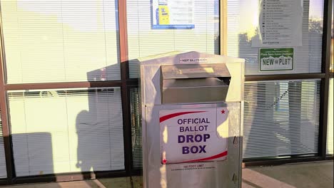 mother teaching daughter how to vote in election at official ballot drop box by casting ballot letter with child for democratic mail-in voting at booth