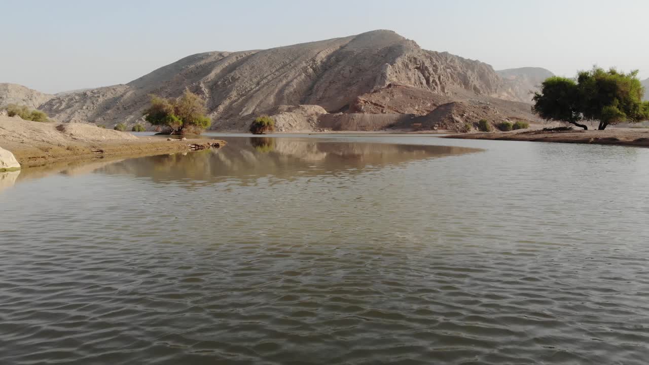 vista aérea que revela un lago aislado rodeado de montañas en fujairah, emiratos árabes unidos durante un cielo despejado por la mañana