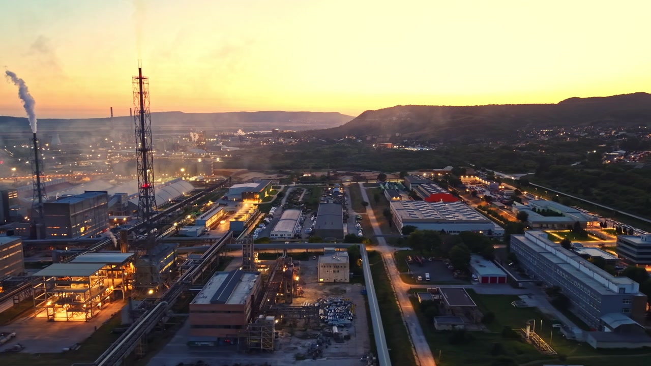 Vista al tramonto di un'area industriale con fabbriche e colline distanti sullo sfondo vicino a una città.
