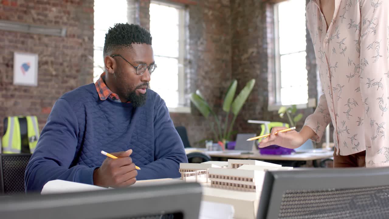 Focused diverse colleagues discussing work at table with building model in office in slow motion