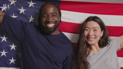 retrato de estudio de una pareja multicultural con una bandera estadounidense detrás de ellos celebrando el 4 de julio, día de la independencia 1