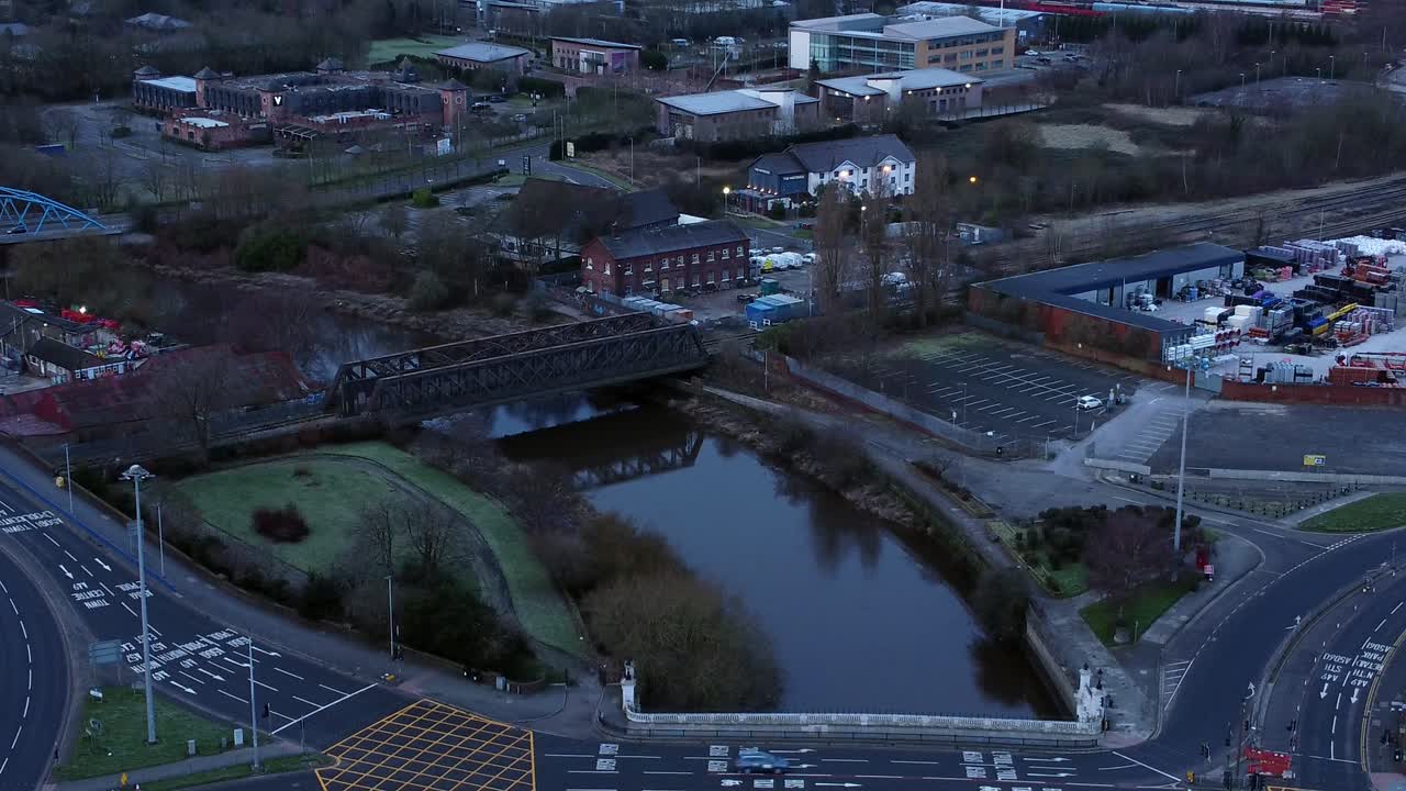 Aerial early morning city street traffic commuting intersection lanes crossing curved river descend to low angle
