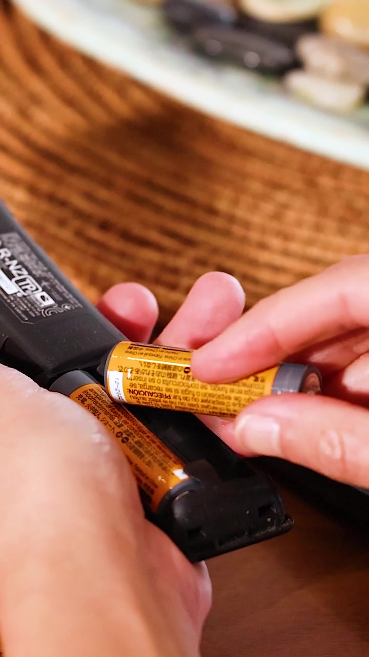 Hands replace batteries in a remote control on a wooden table with natural lighting