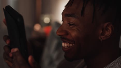 A-Young-black-male-smiles-and-laughs-at-his-tablet-device-while-watching-something