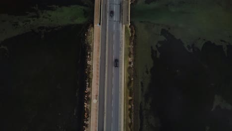 Revele-Autos-Baleados-En-La-Carretera-Del-Puente-Que-Cruza-La-Laguna-Hacia-La-Antigua-Ciudad-Isleña-Orbetello-Cerca-De-Monte-Argentario-Y-El-Parque-Maremma-En-Toscana,-Italia,-Con-Reflejos-En-El-Agua